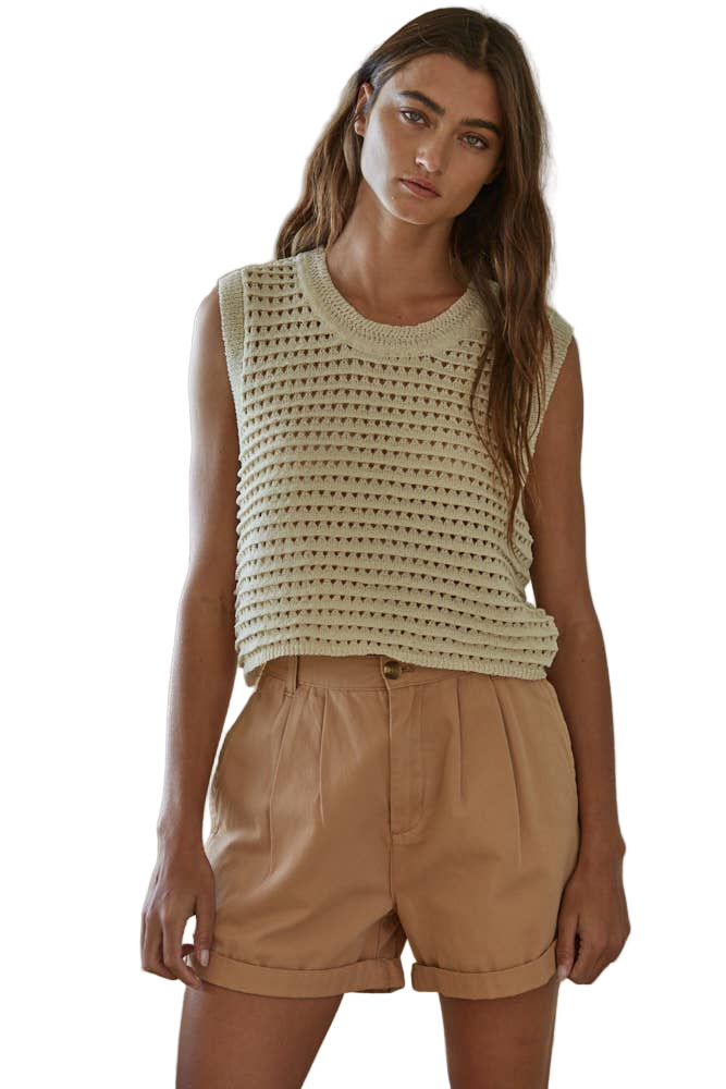 A female model wearing a beige knit sweater with crocheted sleeveless crop top and a round neckline, paired with a brown skirt.