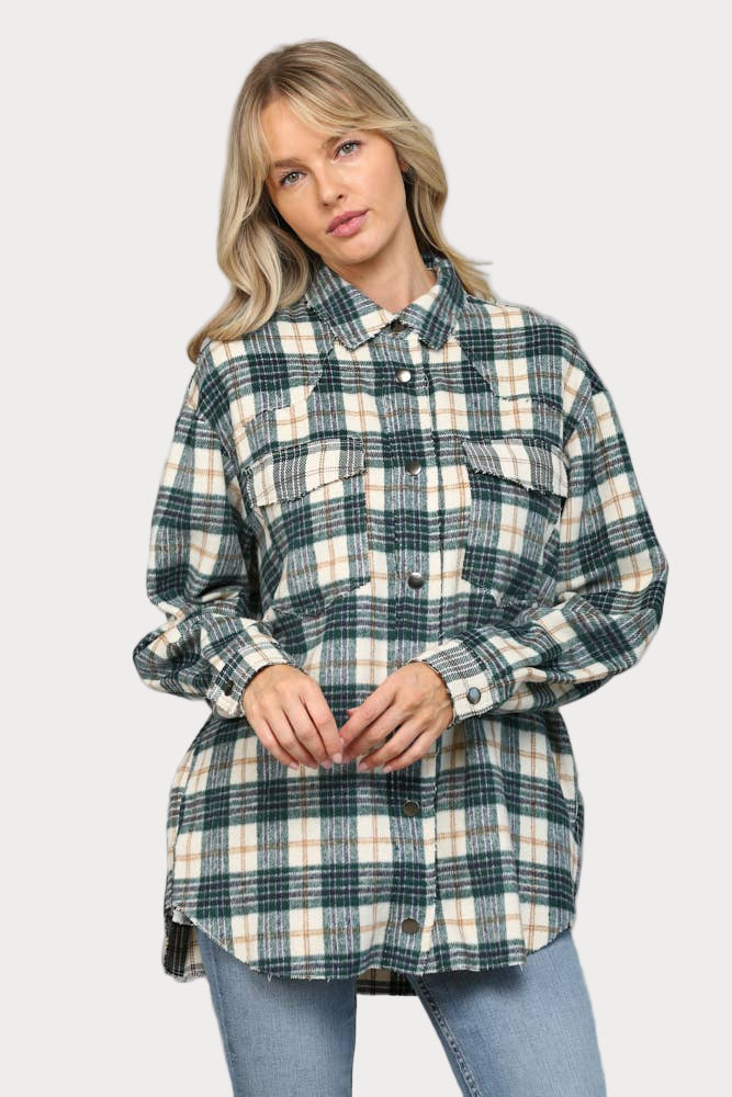 A woman wearing an oversized hunter green, cream, and tan plaid shacket with raw edge chest pockets and snap buttons, paired with light wash jeans.

