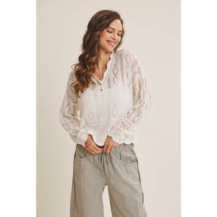 Woman wearing a white open-knit crochet sweater top with scalloped hem and long sleeves
