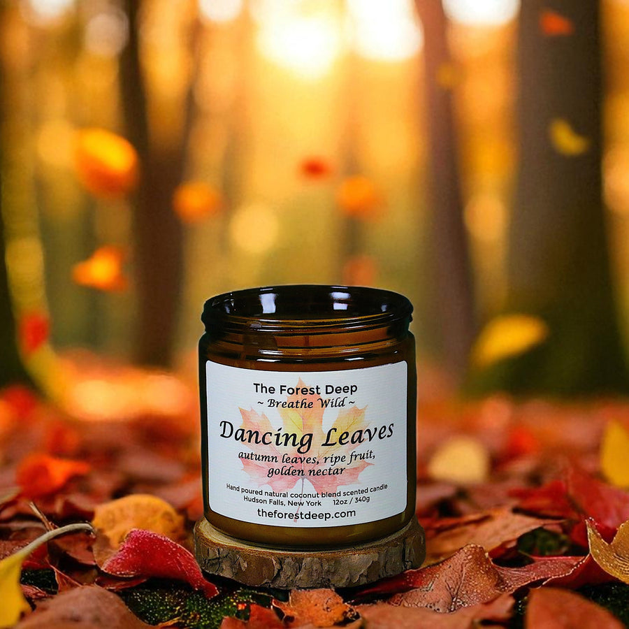 Candle jar labeled 'Dancing Leaves' on a bed of autumn leaves with a forest background