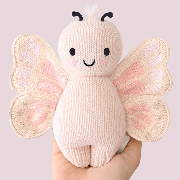 Knitted butterfly toy held in a hand against a light background
