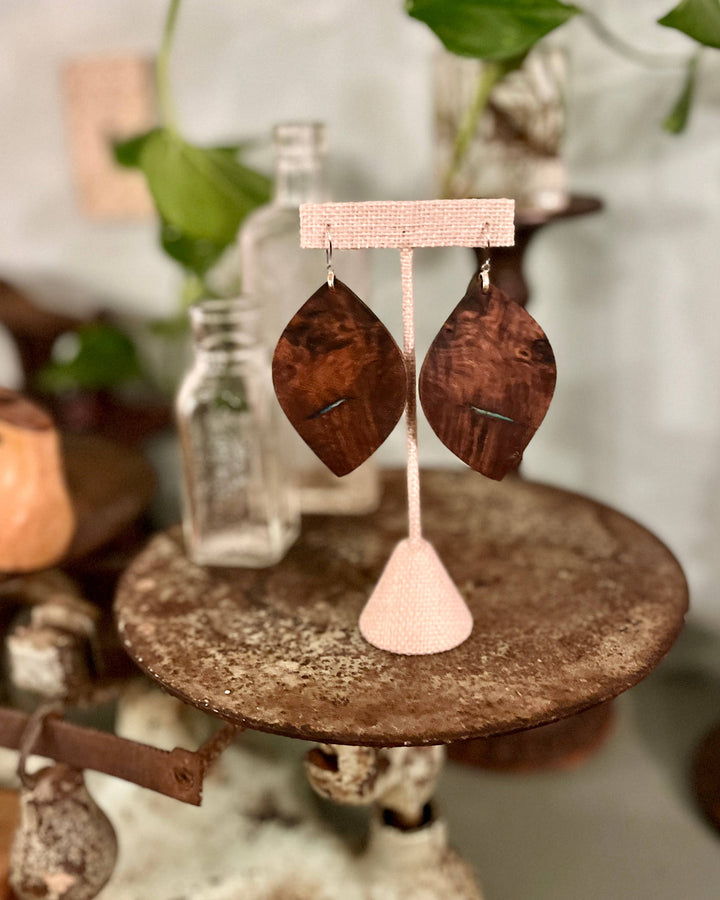 Wooden leaf-shaped earrings on a pink stand with a blurred natural background