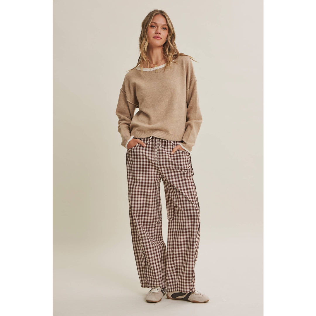 Woman wearing a beige sweater and plaid pants on a plain background