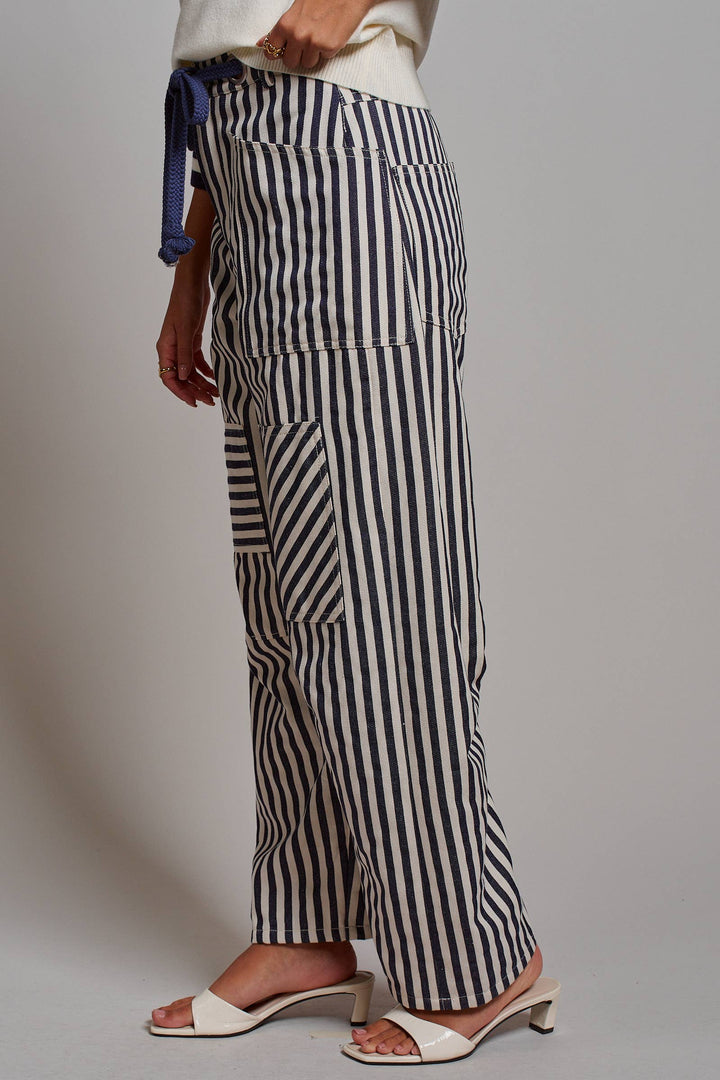 Woman wearing navy and ivory railroad stripe utility pants with oversized patch pockets, braided drawstring waist, and relaxed straight-leg fit.