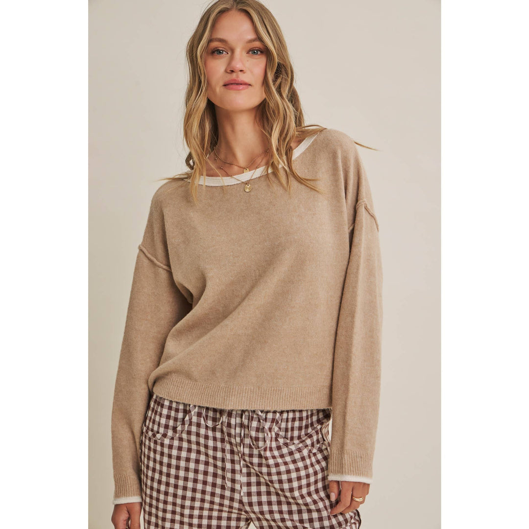 Woman wearing a beige sweater and checkered pants on a plain background