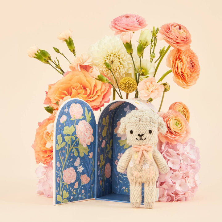 Knitted lamb toy with a floral box and flowers on a beige background