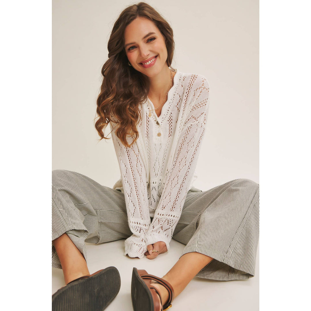 Woman wearing a white open-knit crochet sweater top with scalloped hem and long sleeves