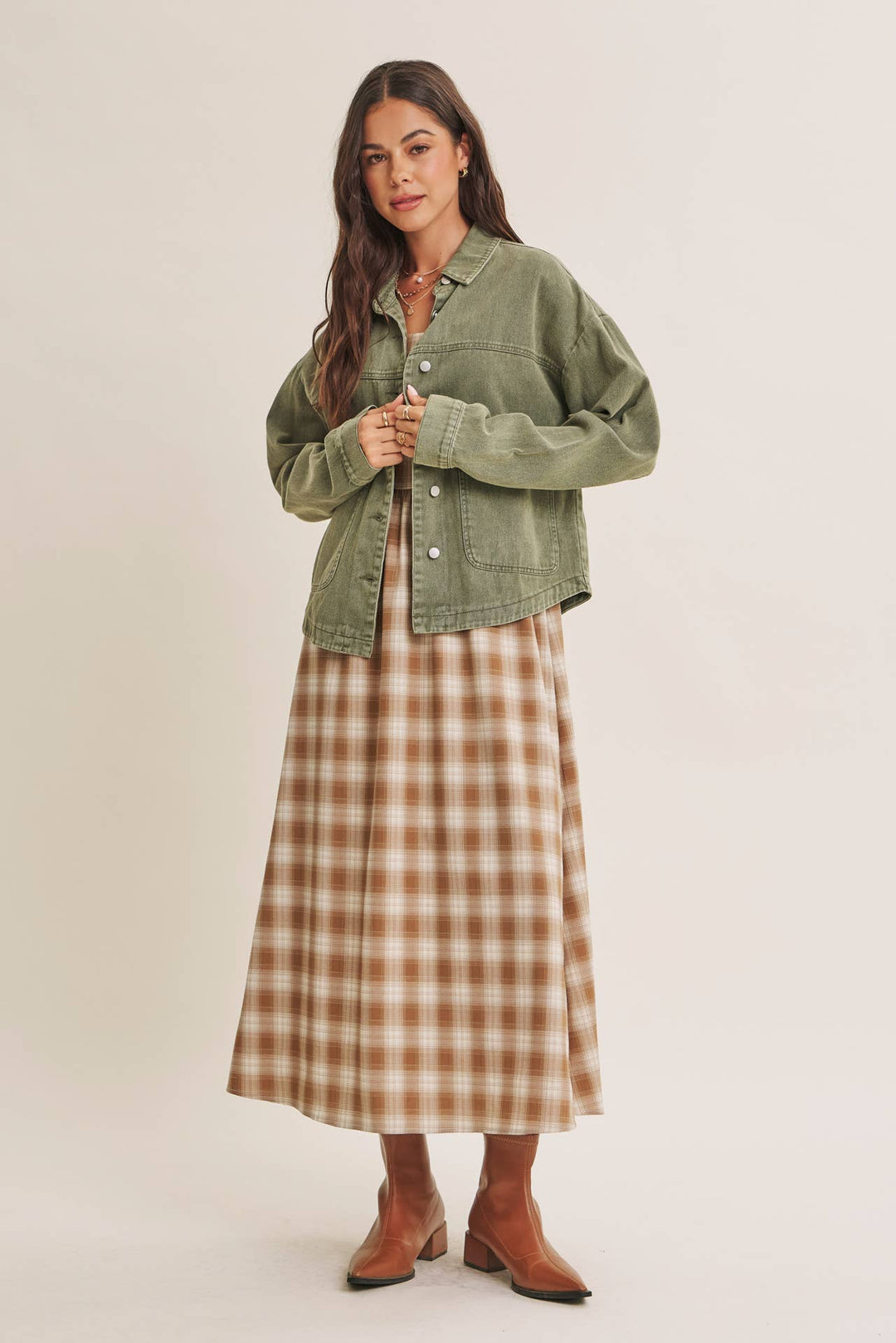 Woman wearing a olive green jacket over a plaid dress on a beige background