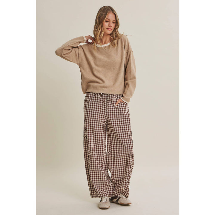 Woman wearing a beige sweater and plaid pants on a plain background