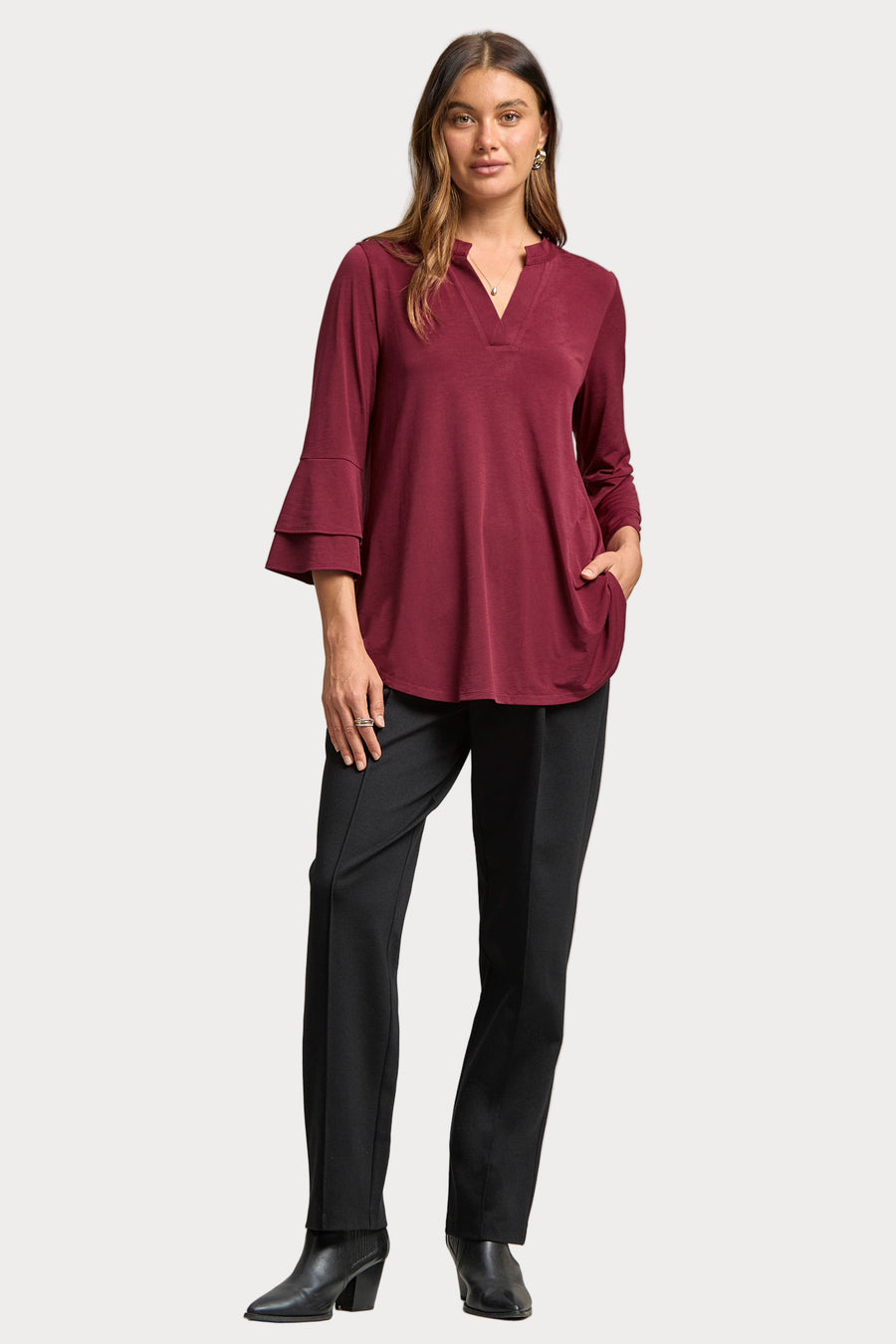 Woman wearing a burgundy top and black pants on a plain background