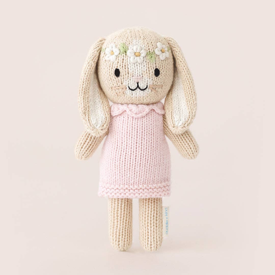 Knitted bunny toy with a pink dress on a beige background