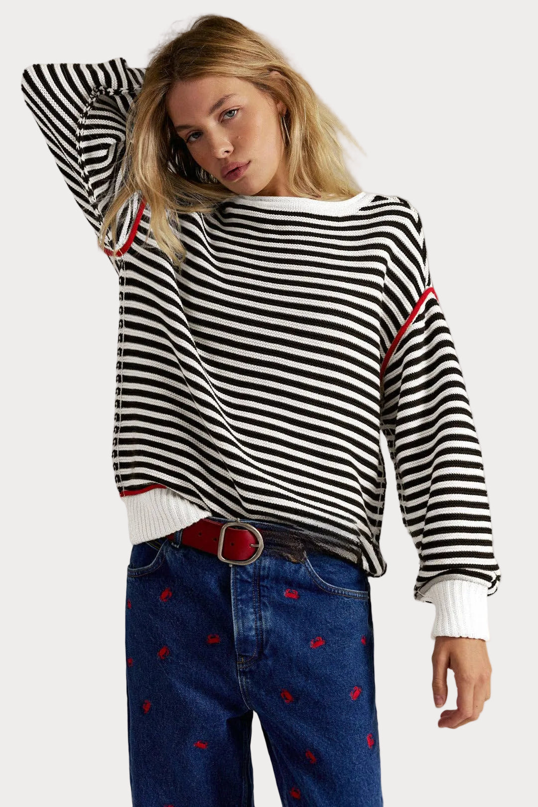 Striped knit sweater pullover with black and cream stripes, red piping details, relaxed fit, and dropped shoulders worn with jeans