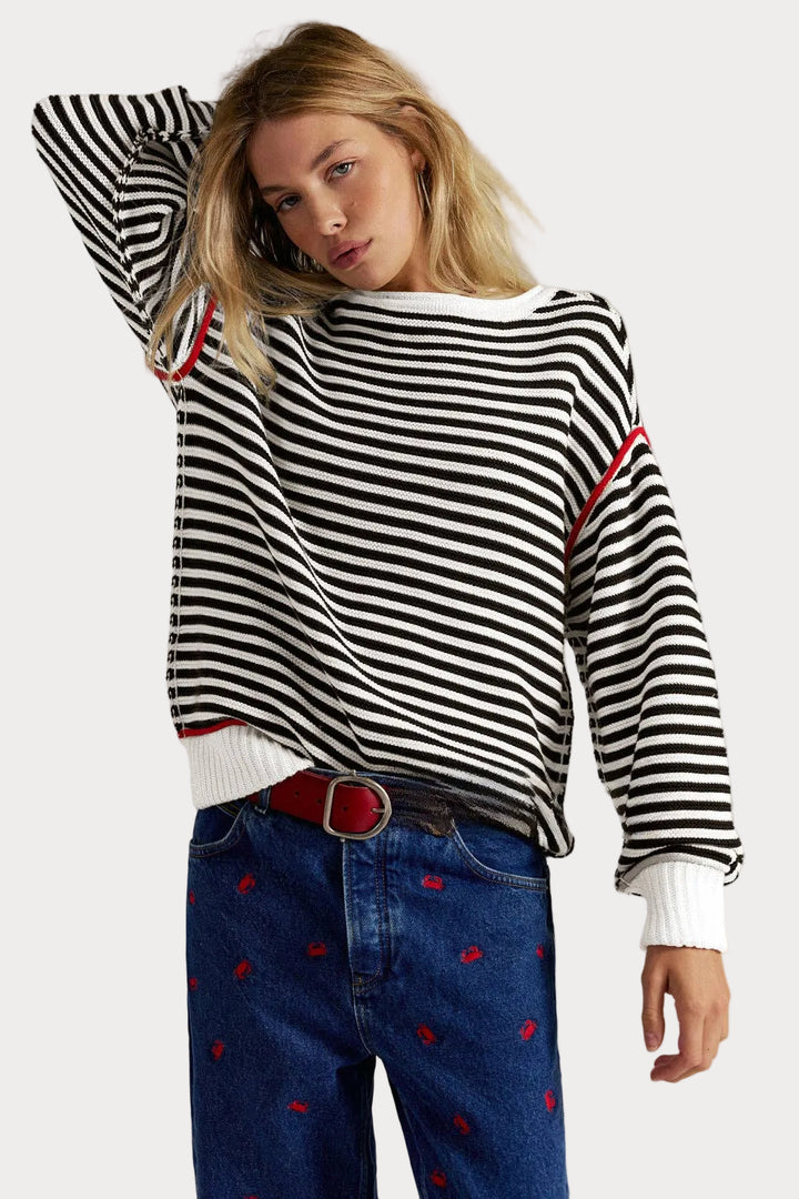 Striped knit sweater pullover with black and cream stripes, red piping details, relaxed fit, and dropped shoulders worn with jeans