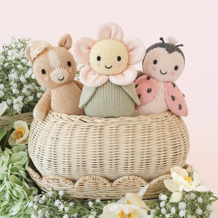 Three knitted toys shaped like a horse, flower, and ladybug in a wicker basket with a floral background.