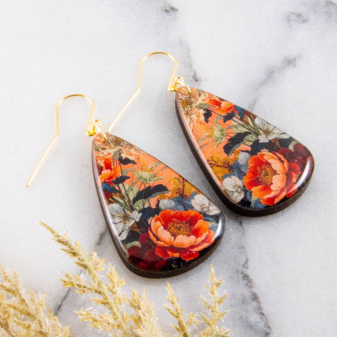 Floral teardrop earrings on a marble surface with dried plants.