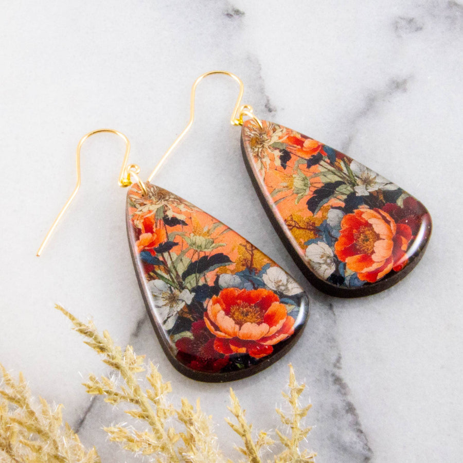 Floral teardrop earrings on a marble surface with dried plants.