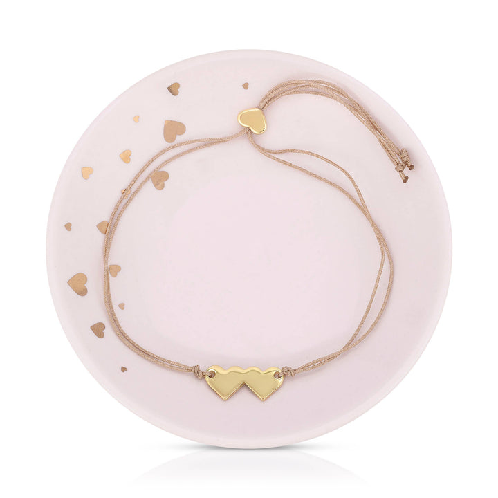 Gold heart-shaped bracelet on a pink ceramic dish with heart patterns