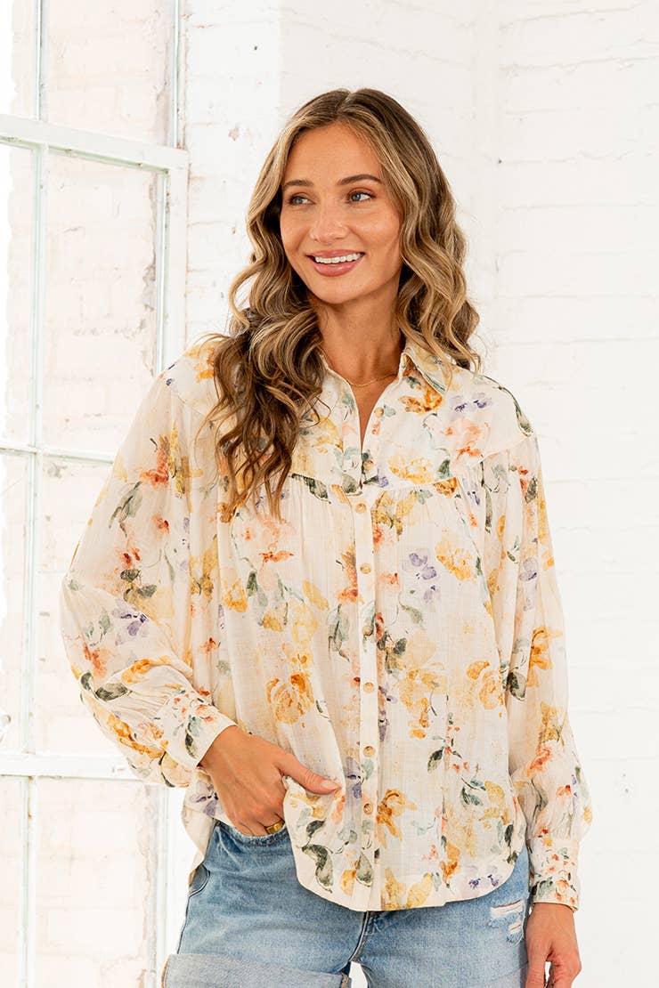 Woman wearing cream watercolor floral button-down blouse with long sleeves and denim shorts