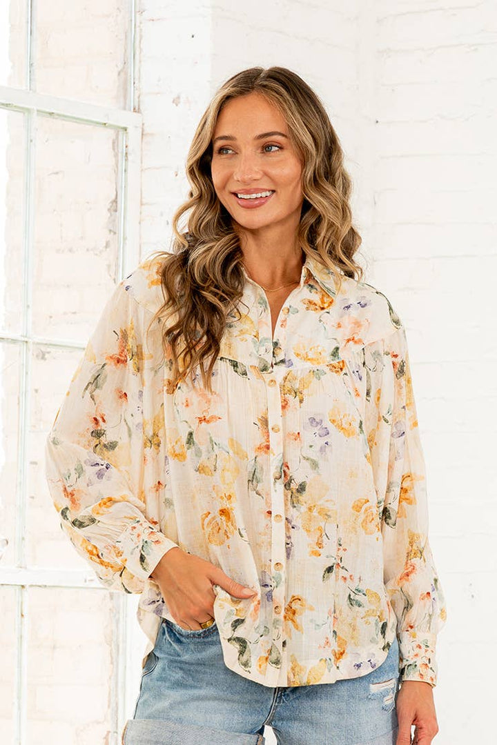 Woman wearing cream watercolor floral button-down blouse with long sleeves and denim shorts