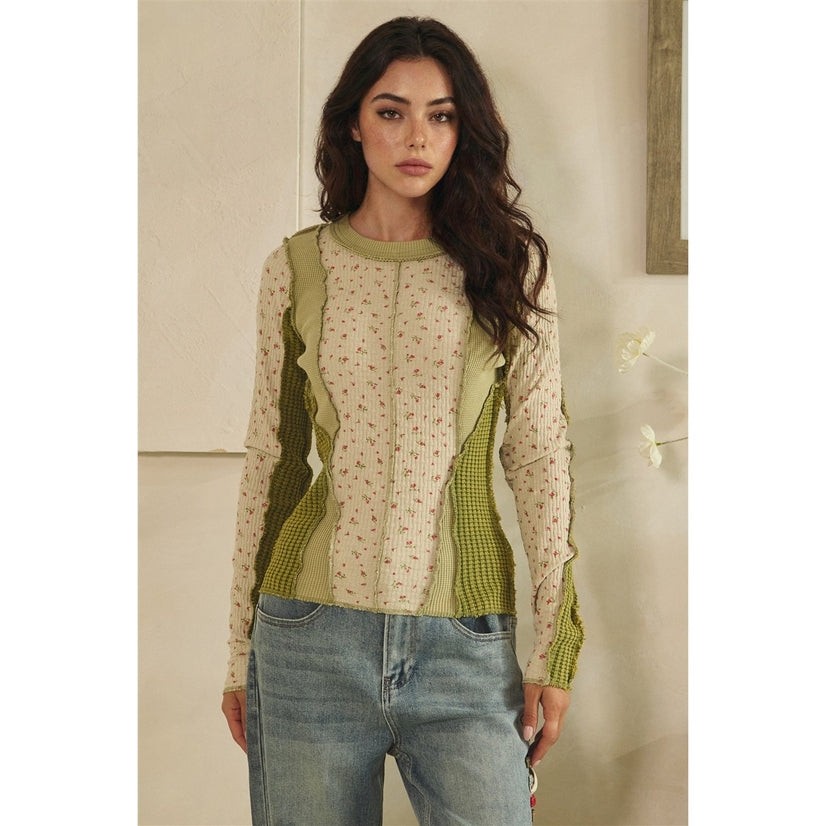 Woman wearing a green and beige top with floral pattern, standing indoors.