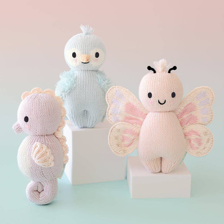 Three knitted toys: a butterfly, a seahorse, and a bird on a light pink background.