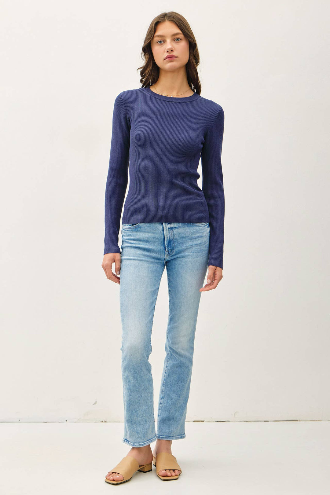 Woman wearing a blue long-sleeve top and light blue jeans on a white background