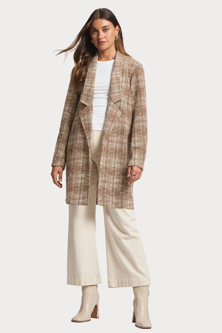 Woman wearing a plaid coat, white top, beige pants, and boots on a white background
