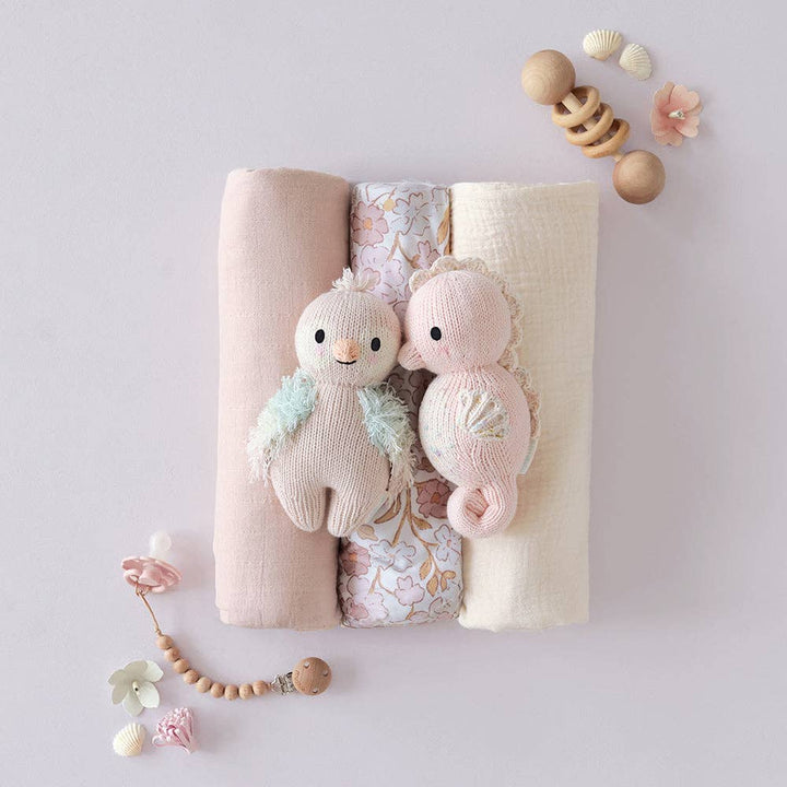 Two knitted toys on a floral blanket with wooden beads and flowers on a light gray background