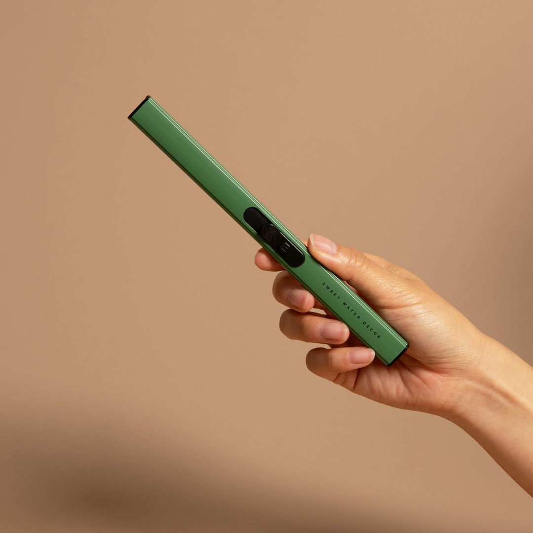 A hand holding a slim green electronic lighter against a solid warm beige background.