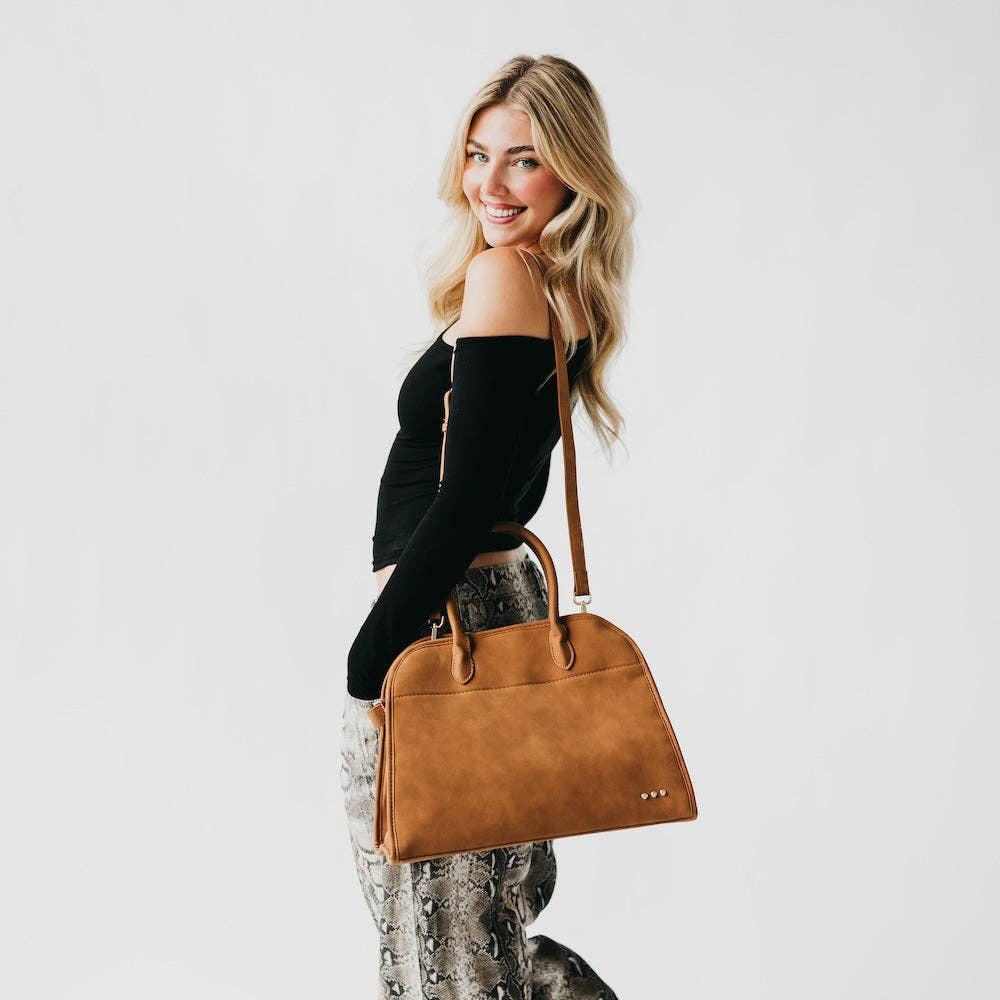 Woman holding a brown leather handbag against a plain background
