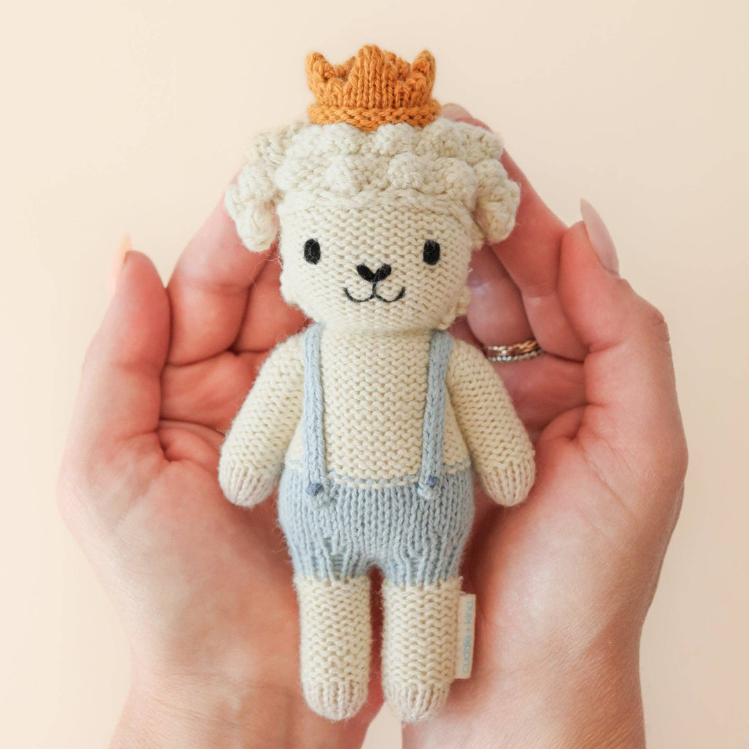 Knitted toy lamb with a crown held in a hand against a beige background