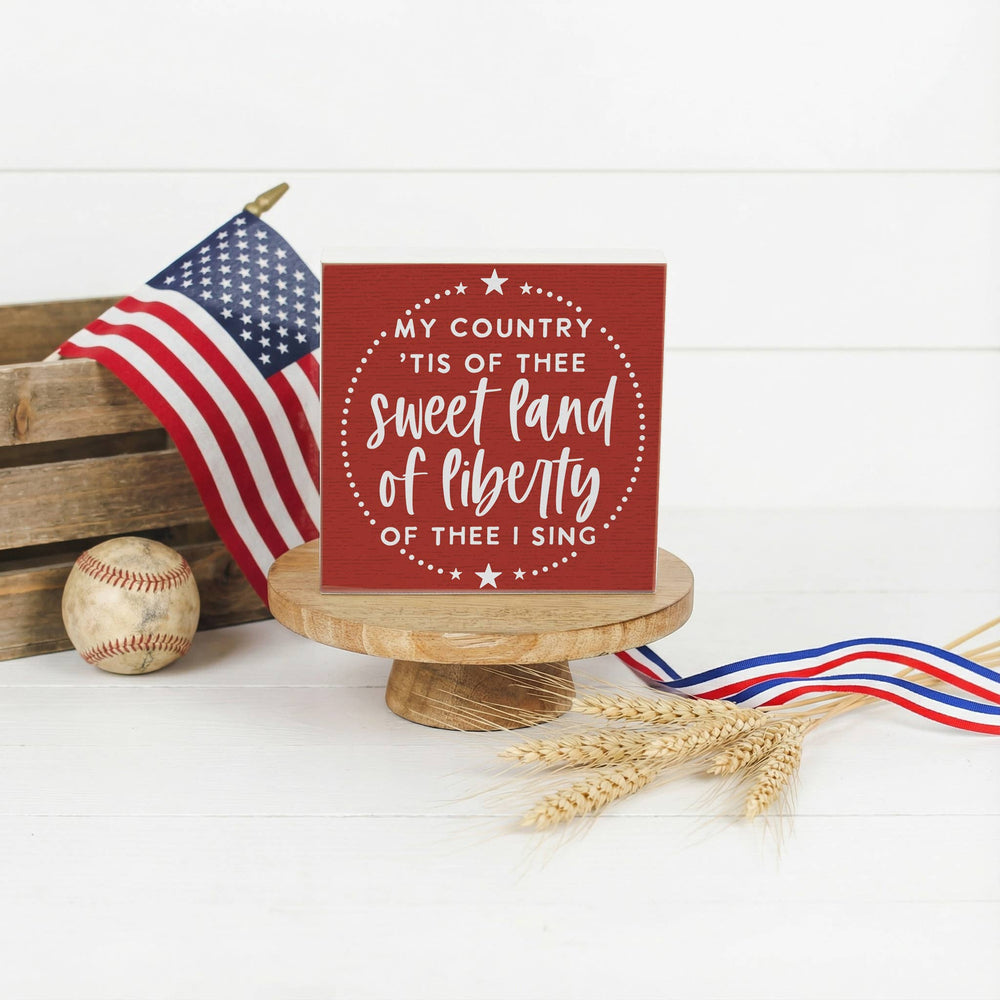 Small red sign with patriotic quote, American flag, baseball, and wheat on a white background