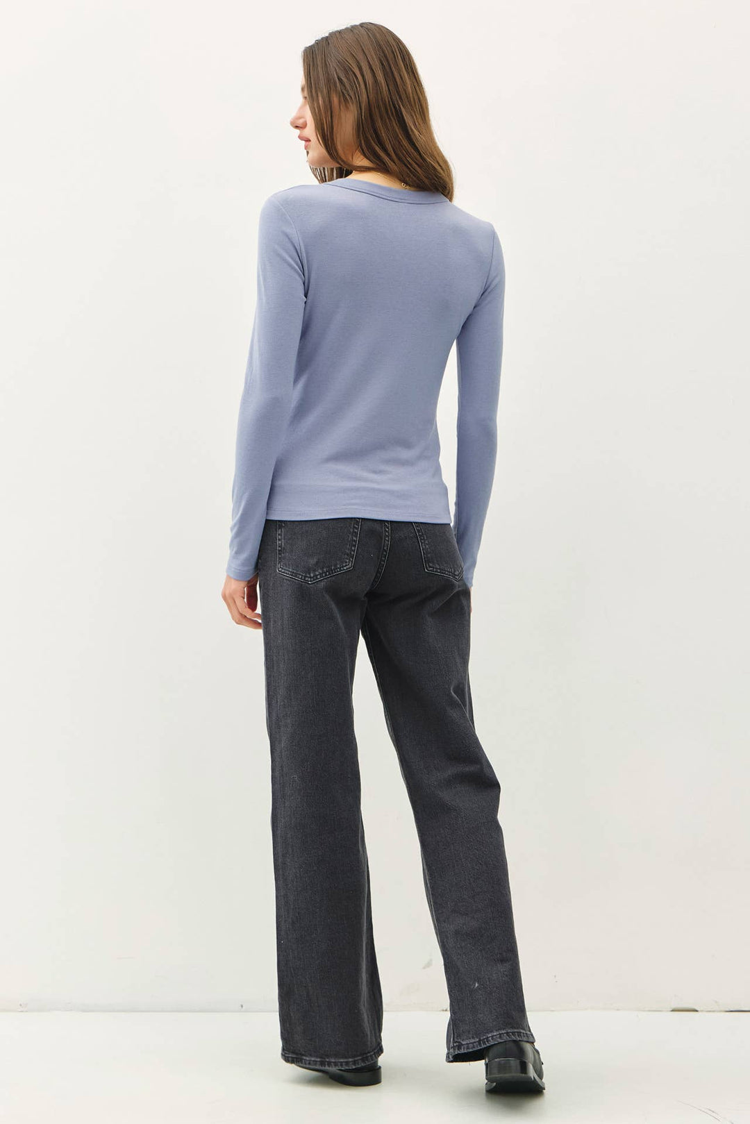 Person wearing a light blue long-sleeve shirt and dark jeans on a white background