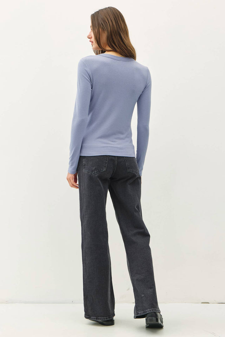 Person wearing a light blue long-sleeve shirt and dark jeans on a white background