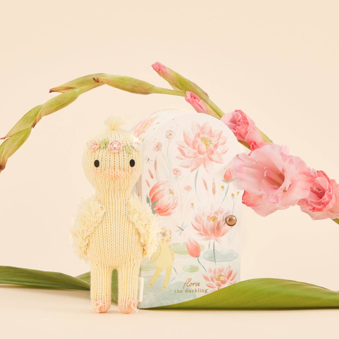 Knitted duckling toy with floral packaging and pink flowers on a beige background