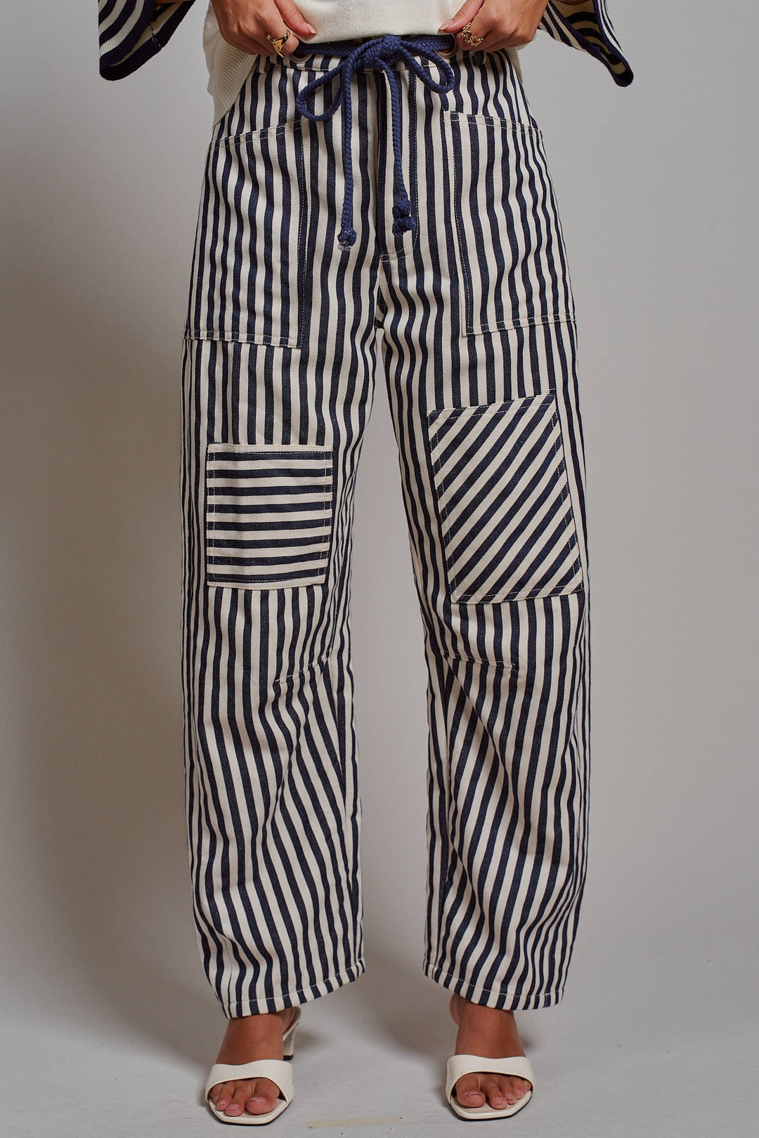 Woman wearing navy and ivory railroad stripe utility pants with oversized patch pockets, braided drawstring waist, and relaxed straight-leg fit.