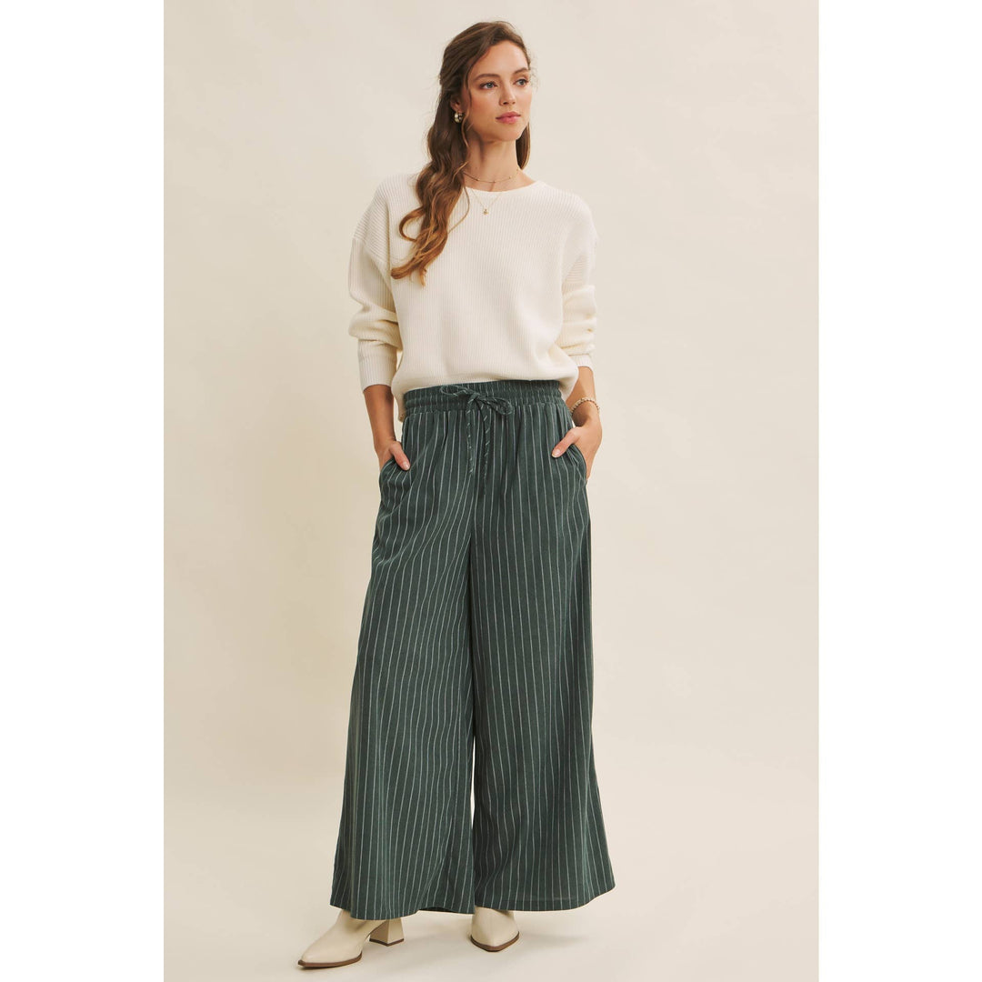 Woman wearing Bow Back Sweater | Dolman Sleeve Knit with Satin Tie and green striped pants on a beige background