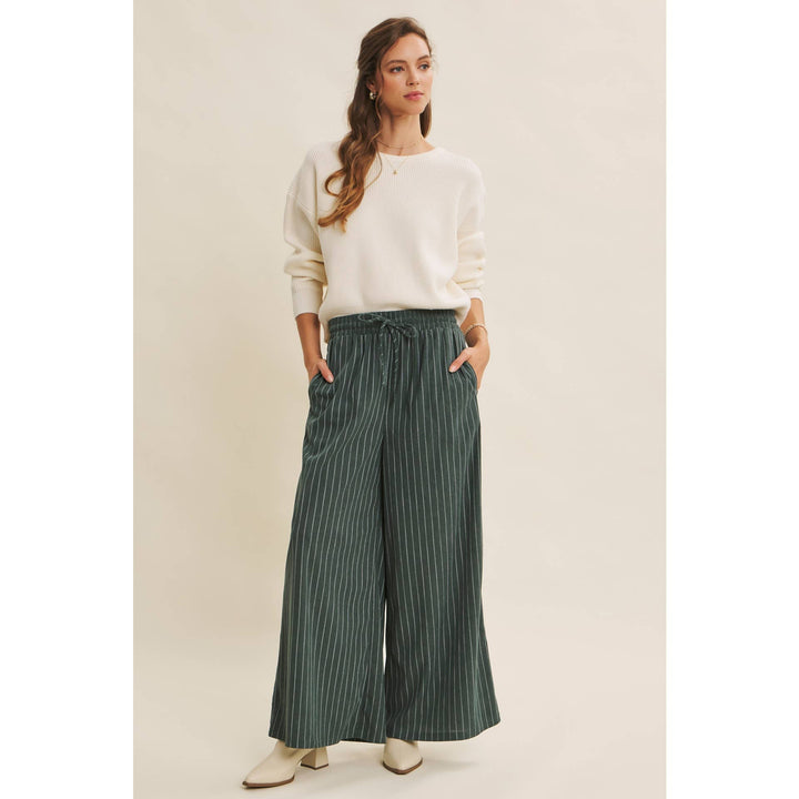 Woman wearing Bow Back Sweater | Dolman Sleeve Knit with Satin Tie and green striped pants on a beige background