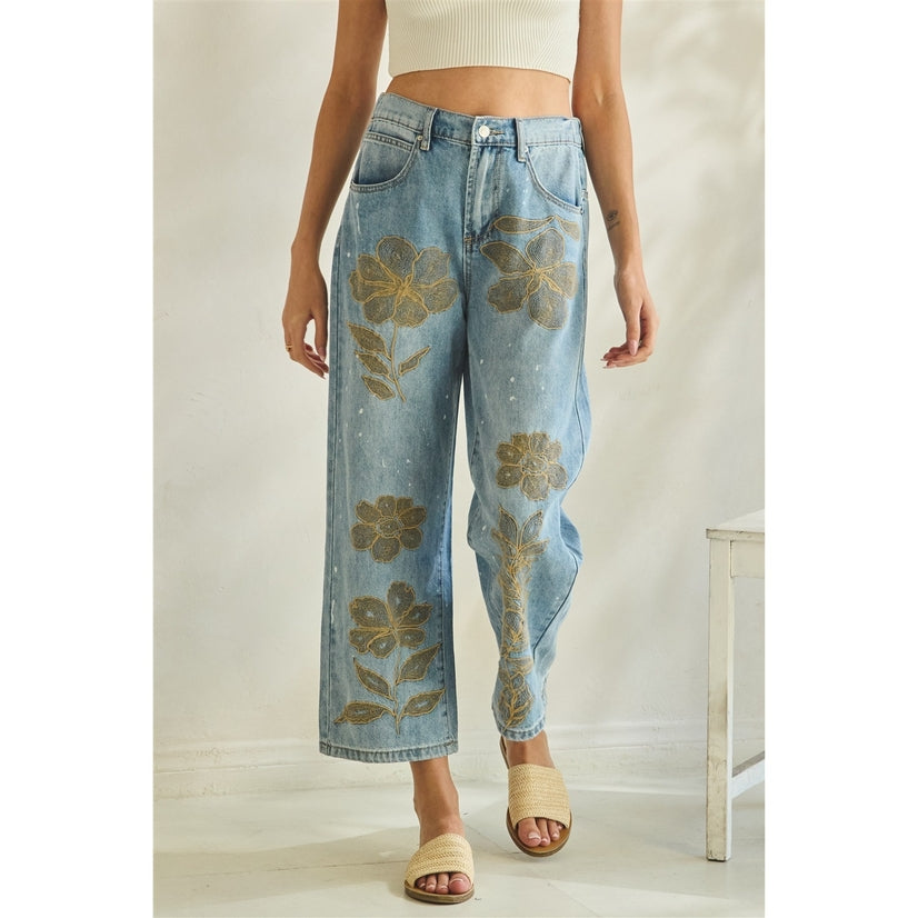 Denim jeans with floral embroidery worn by a person on a neutral background