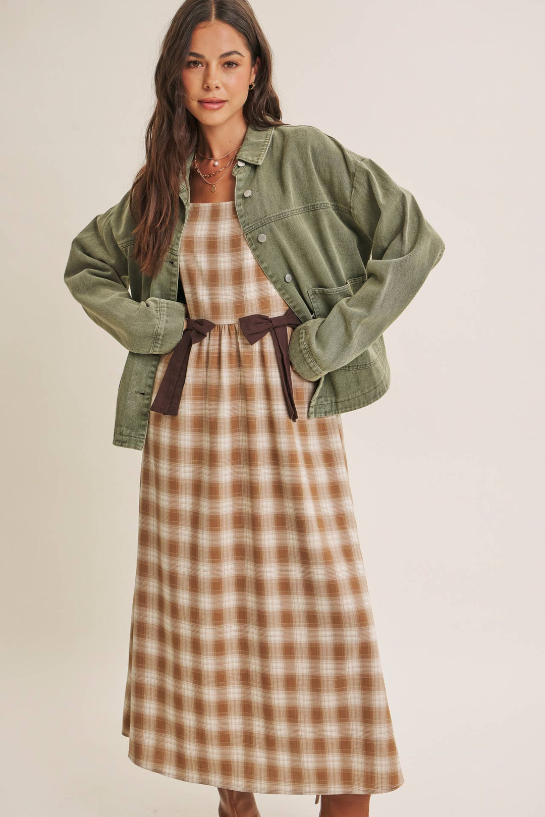 Woman wearing a olive green jacket over a plaid dress on a beige background