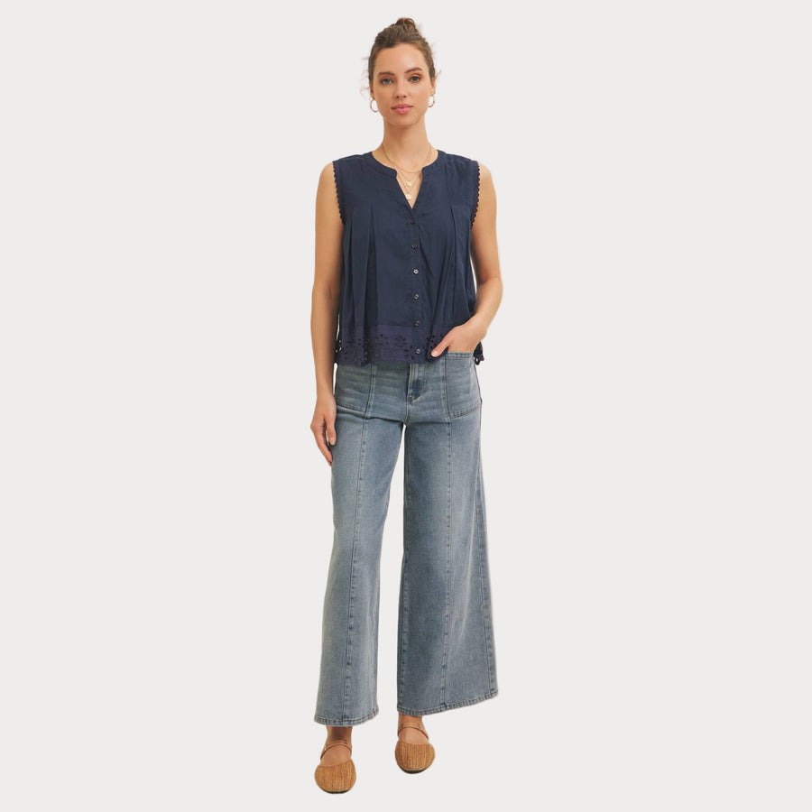 Woman wearing a navy sleeveless top and light blue jeans against a beige background