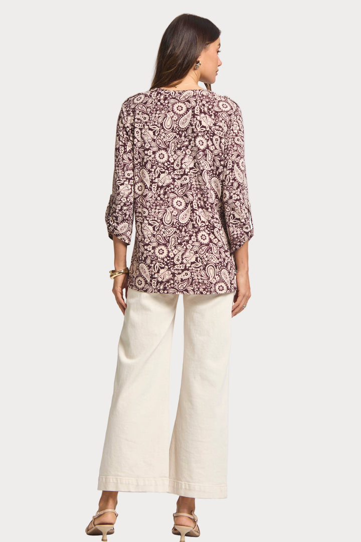 Woman wearing a patterned blouse and white pants on a white background