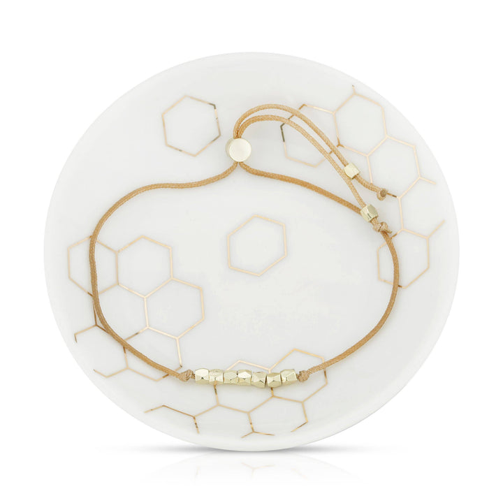 Gold bracelet on a white dish with honeycomb patterns