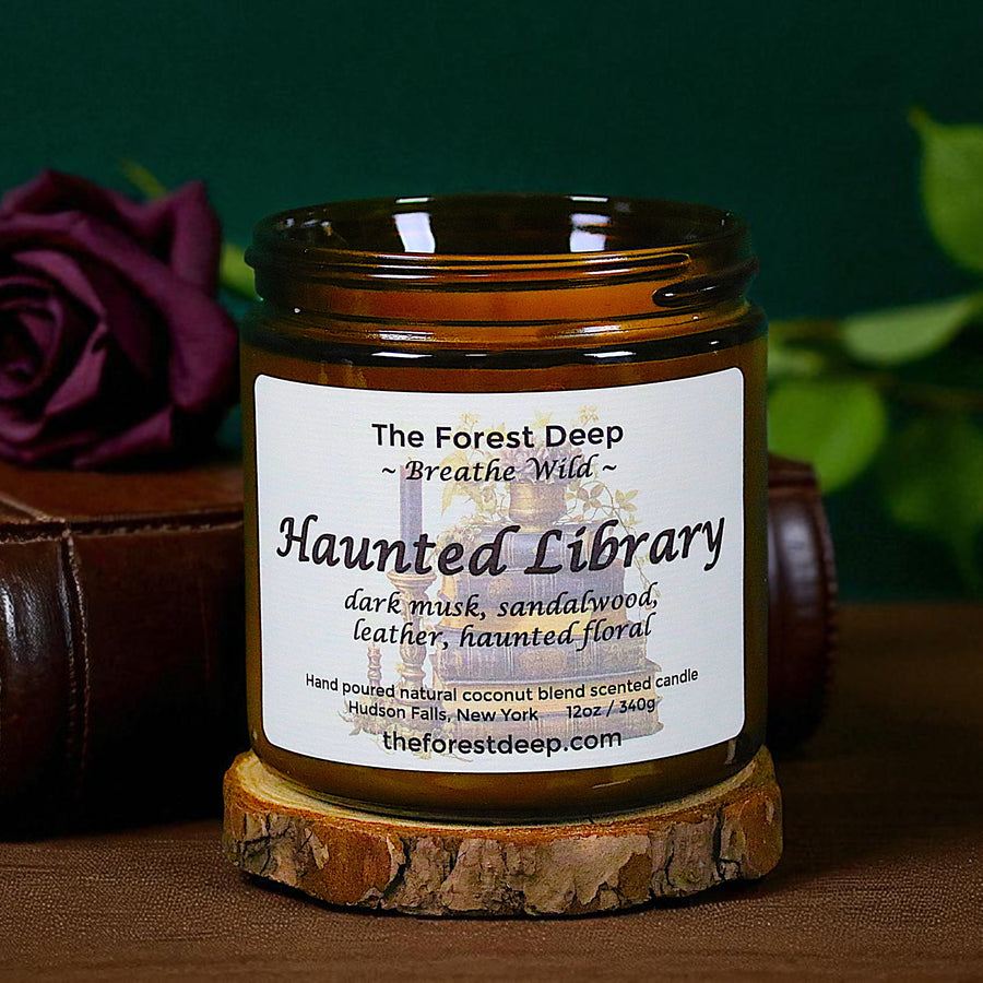 Candle labeled 'Haunted Library' on a wooden base with a purple rose and book in the background.