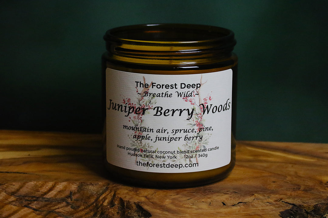 Amber jar candle labeled Juniper Berry Woods on wooden surface