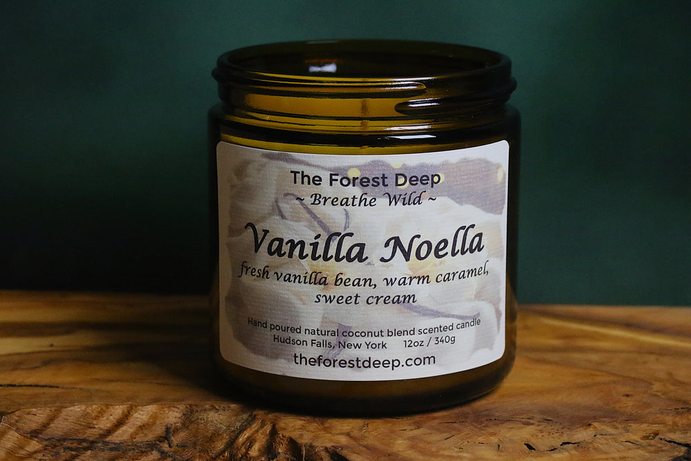 Amber jar candle labeled Vanilla Noella on wooden surface