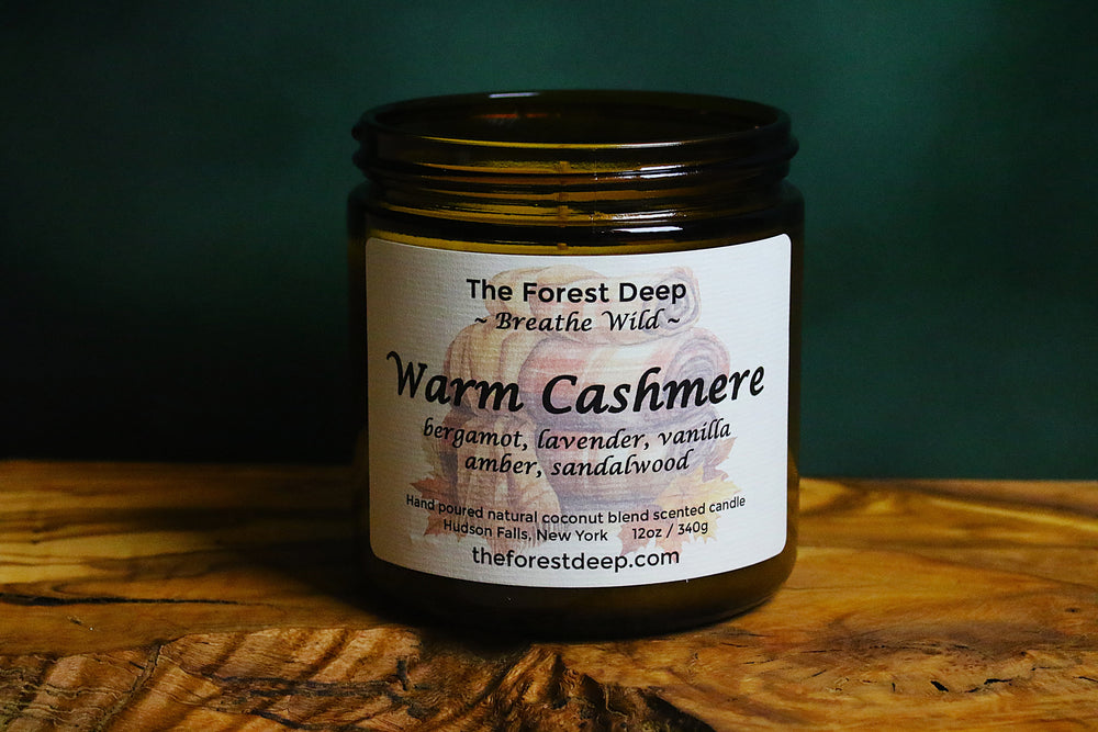 Amber glass candle labeled Warm Cashmere with notes of bergamot, lavender, vanilla, amber, and sandalwood