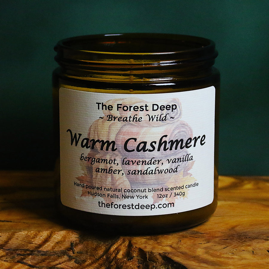 Amber glass candle labeled Warm Cashmere with notes of bergamot, lavender, vanilla, amber, and sandalwood